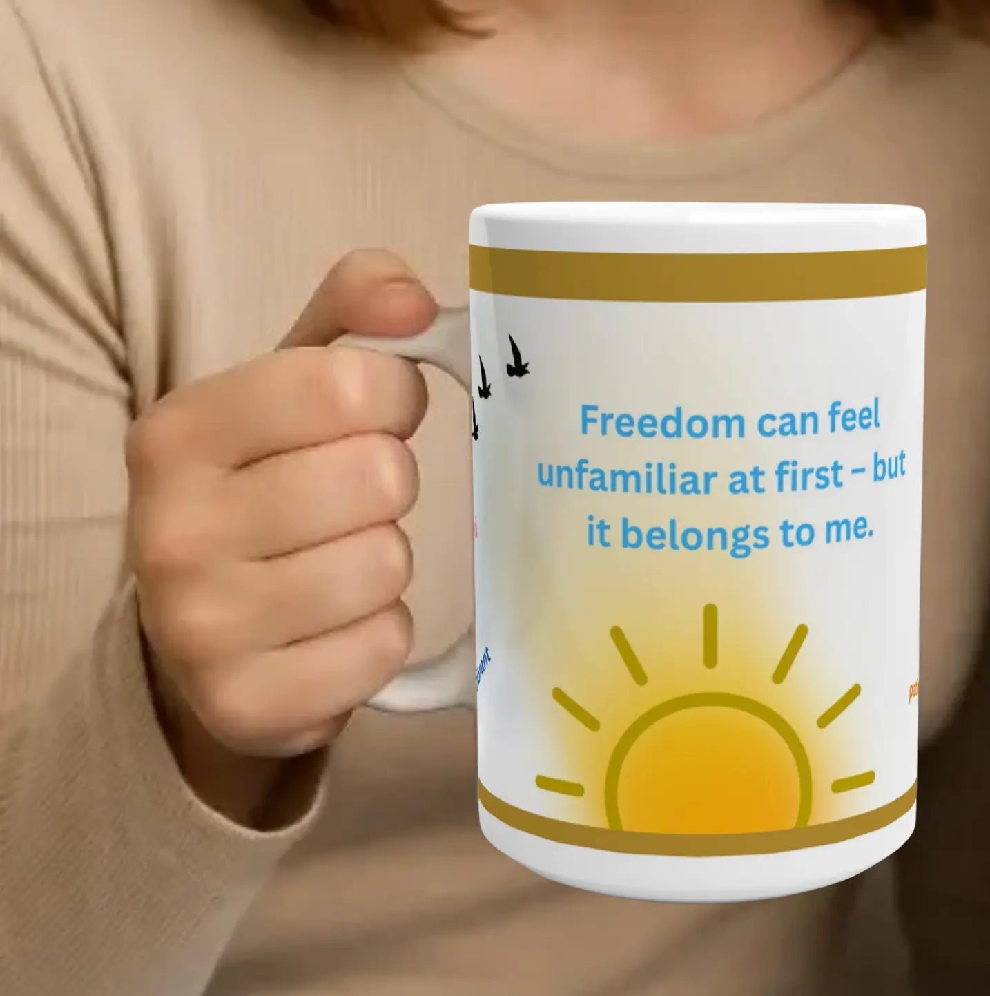 Eine Person hält eine Tasse mit dem Text 'Freedom can feel unfamiliar at first - but it belongs to me.' Auf der Tasse sind eine Sonne und Vögel abgebildet.